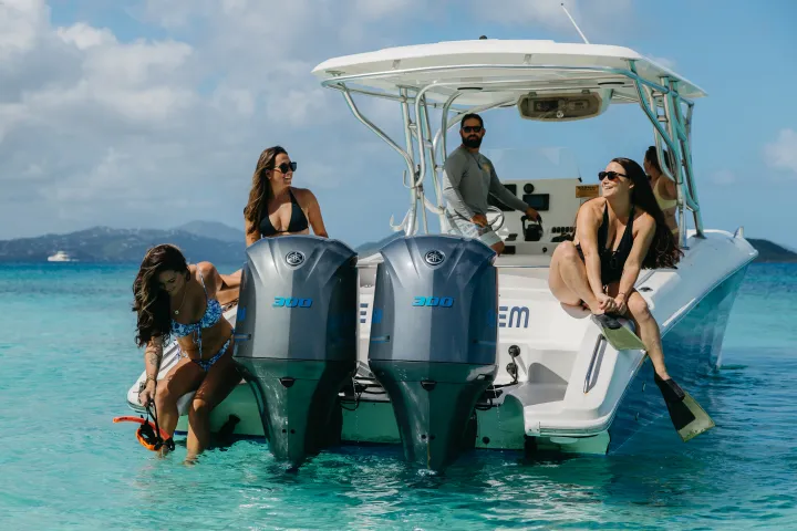 People on a boat in clear blue water, with two outboard motors and distant islands visible.