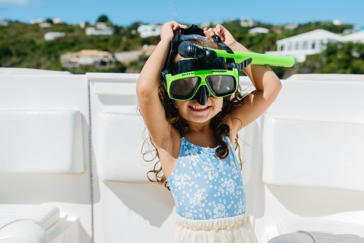 Child on boat wearing a snorkel mask and sunscreen, smiling with arms raised.